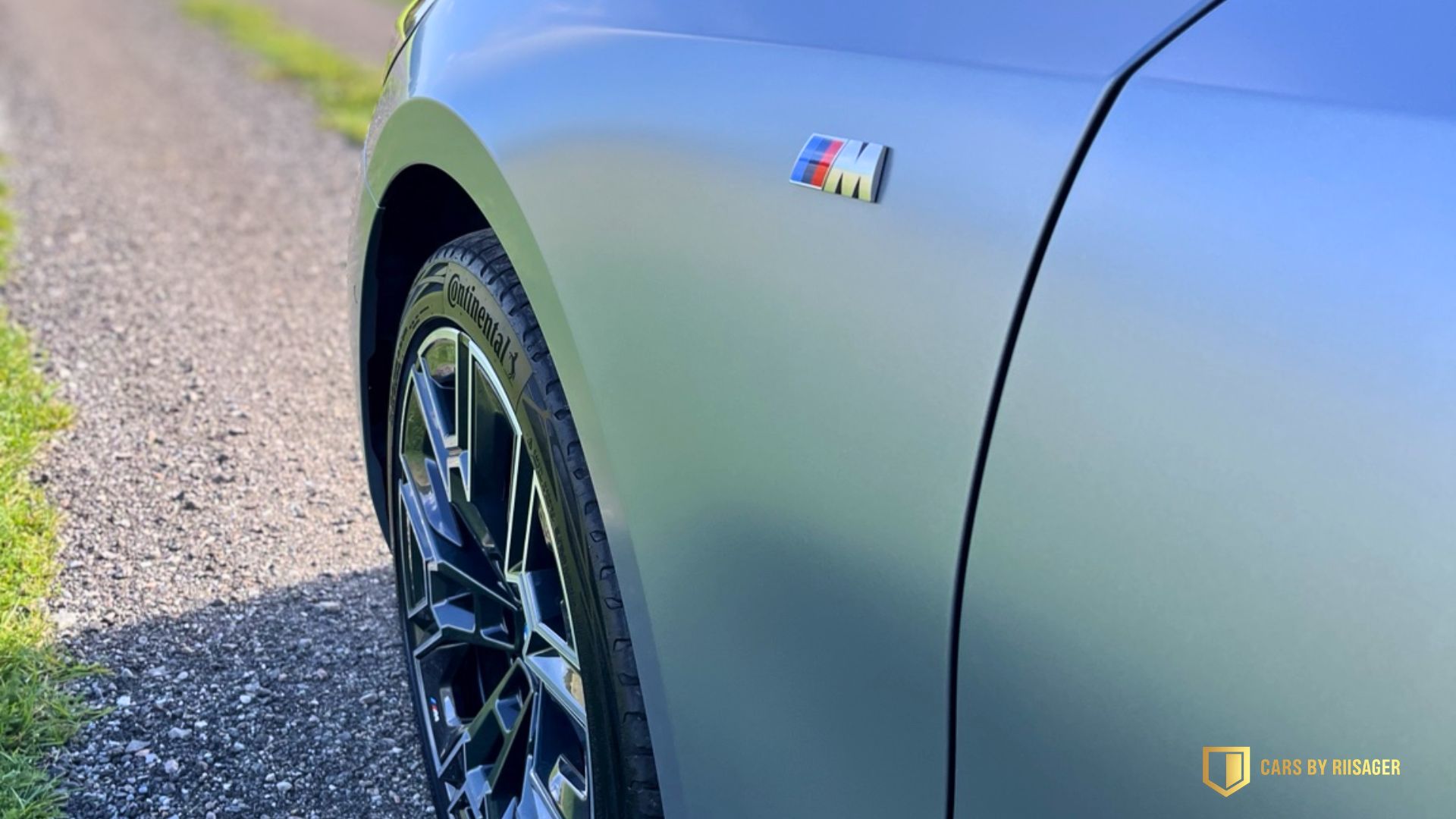 Mat grå forskærm på BMW i5 Touring med M-emblem og en del af forhjulet.
