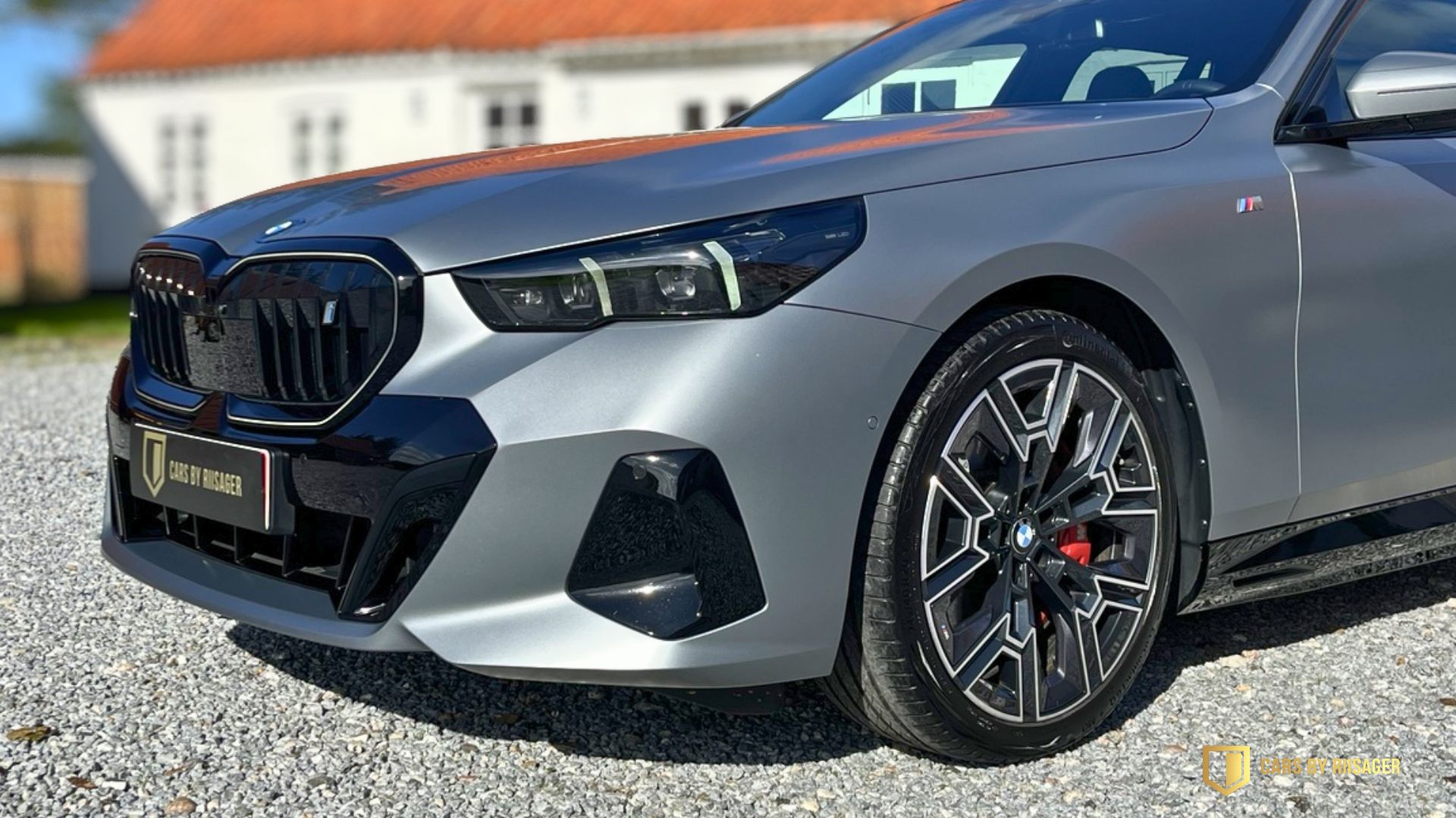 Mat grå forskærm på BMW i5 Touring med M-emblem og en del af forhjulet.